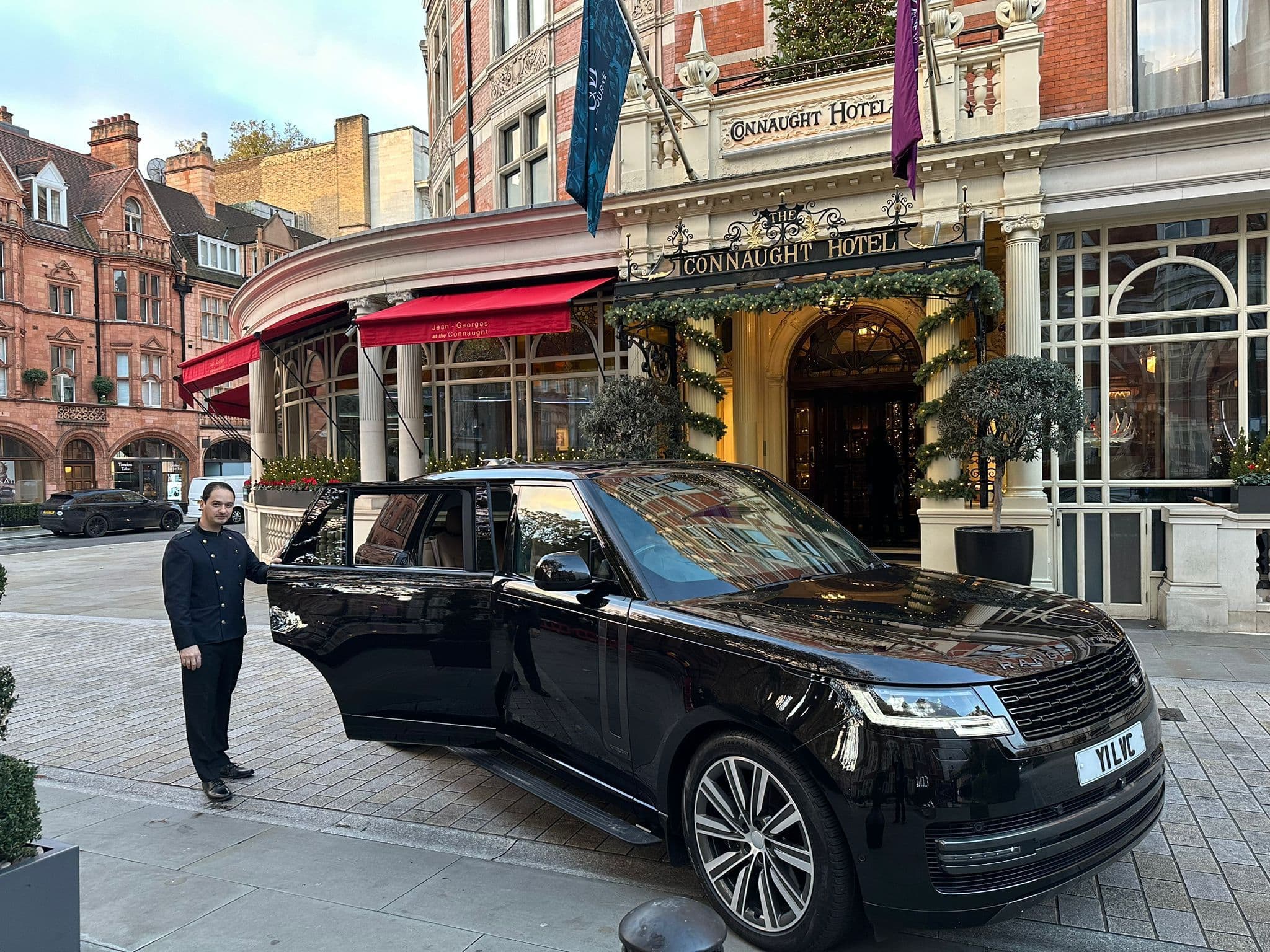 Luxury chauffeur service in London providing VIP hotel pickup with professional porter opening car door for arriving guests